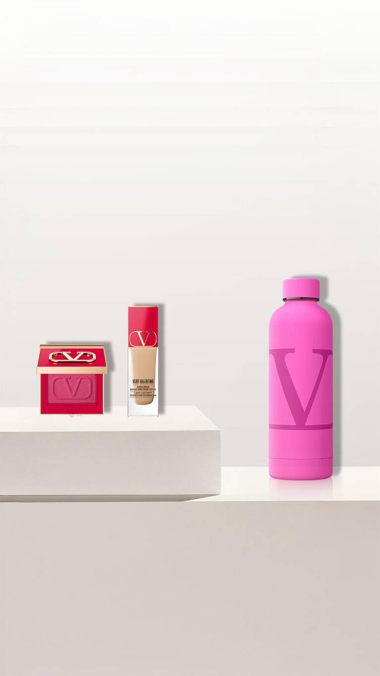A soft pink cosmetic bag with the initials 'VD' beside three perfume bottles on a clean, minimalist display.